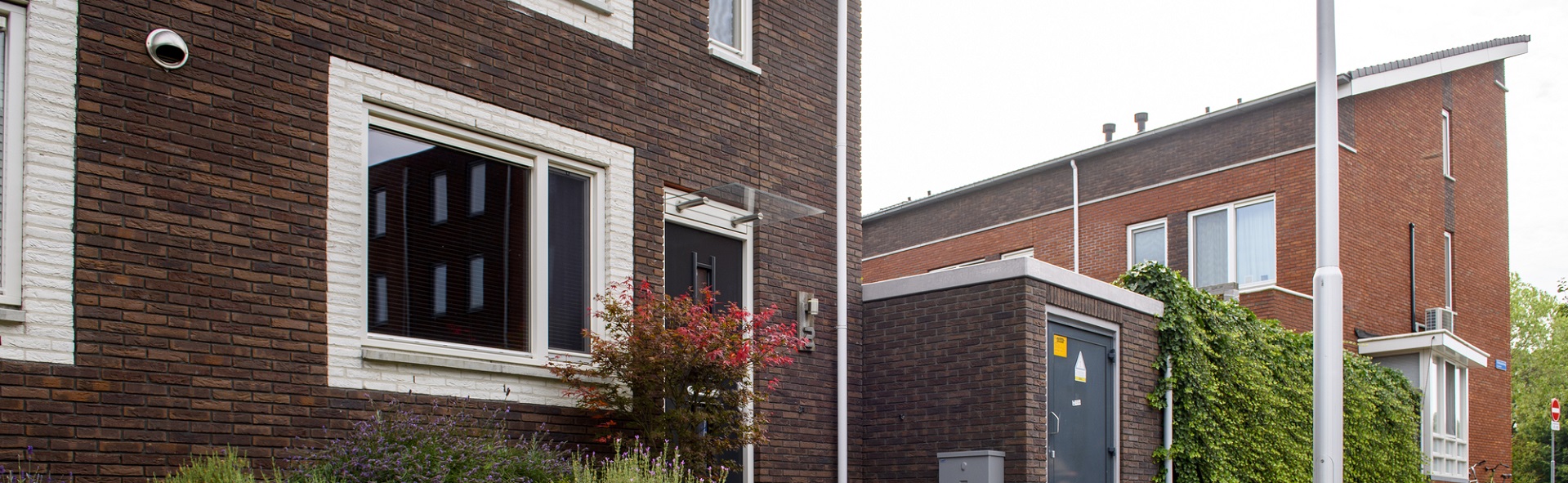 Voorkant van een huis met ernaast een transformatorhuisje
