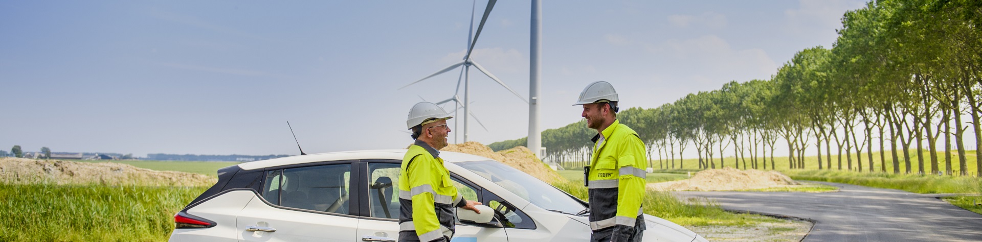Stedin monteurs in gesprek bij auto en windmolens op de achtergrond