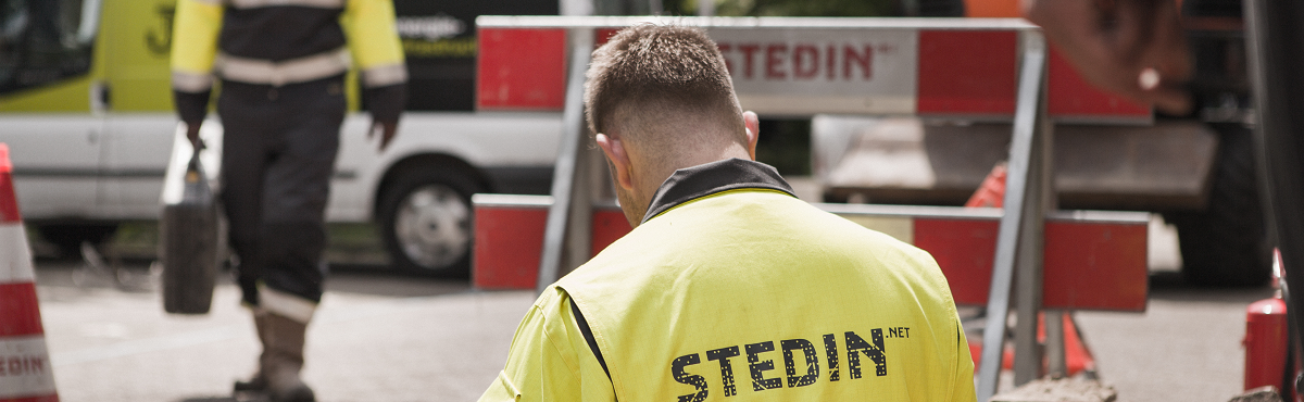 Monteurs van Stedin aan het werk in de straat met op de achtergrond een hekwerk van Stedin