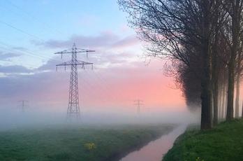 Hoogspaningsmast in weiland met mist, water en zonsopkomst