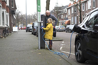 Vader en dochter laden elektrische auto op bij een publieke laadpaal