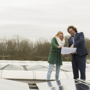 Vrouw en man op een dak met zonnepanelen, bekijken een stuk papier.
