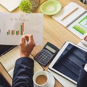 Tafel met calculator, koffie en papierwerk met grafiek waar iemand met pen naar wijst