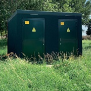 Elektriciteitshuisje in het gras omringd met bomen